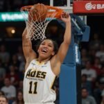 A’ja Wilson, wearing a white Las Vegas Aces jersey, dunks the basketball during a game against the Chicago Sky with an energized crowd in the background.
