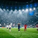 Football players on pitch during European night match with packed stadium
