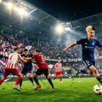 Footballer in blue jersey dribbling ball during night stadium match