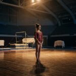 Young gymnast standing alone in large indoor gymnasium with equipment